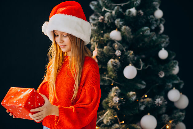欢呼可爱的少女戴着圣诞树旁的红色圣诞帽可爱欢乐圣诞