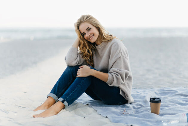 欢呼迷人的白种女人在秋天的海滩上发冷迷人的卷发女模特在沙滩上喝咖啡寒冷卷发沙滩