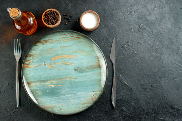 盐顶视图圆形餐盘刀叉黑色胡椒粉和盐油瓶放在黑色桌子上 有自由空间叉子观点碗