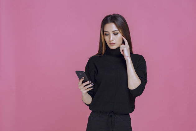 移动穿着黑色毛衣的女人拿着智能手机发短信或查看社交媒体女性成人年轻