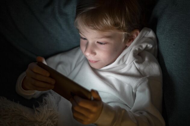 业余爱好男孩晚上在床上用智能手机娱乐移动男孩