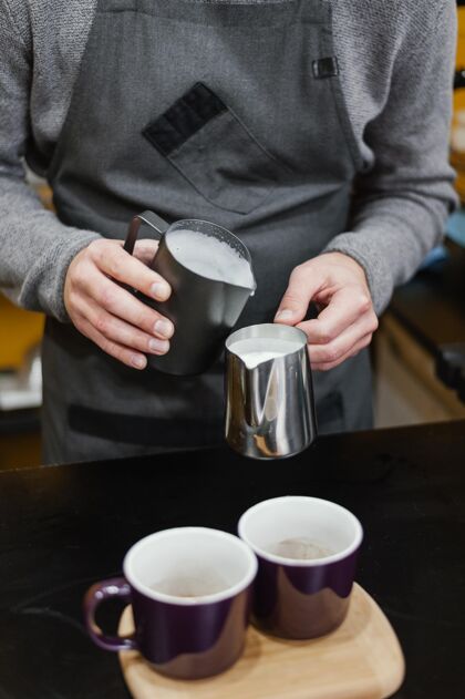 咖啡师男咖啡师在杯子里倒牛奶泡沫的正面图雇员咖啡店咖啡馆