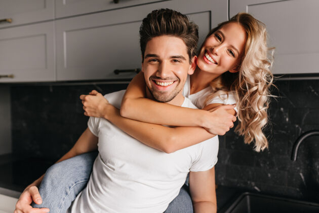 女性快乐的卷发女孩拥抱着丈夫微笑的夫妇在厨房里合影爱公寓快乐