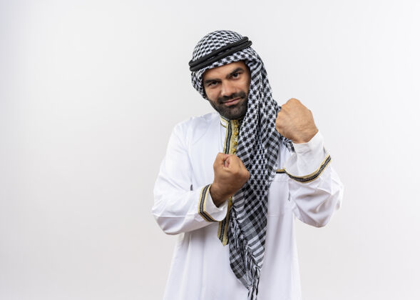 拳头身着传统服装的阿拉伯男子握紧拳头 站在白色的墙壁上开心而积极地微笑着穿积极阿拉伯语