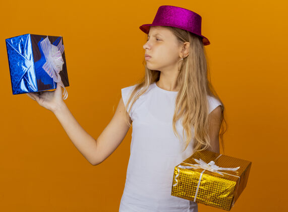 女孩戴着节日帽子拿着礼品盒的漂亮小女孩不高兴小站着