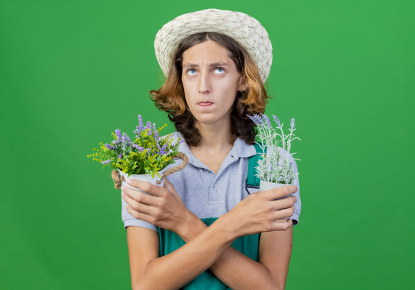 花园年轻的园丁 穿着连体衣 戴着帽子 手里拿着盆栽植物 抬起头来拼图帽子起来