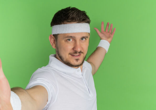 男人身穿白衬衫 头戴头巾的年轻健身男子面带微笑 友好地站在绿色的墙上姿势健身看