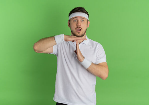 手势身穿白衬衫 头戴头巾的年轻健身男子站在绿色的墙壁上 做出暂停的手势教练健身男性