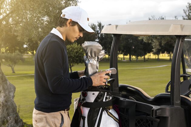 俱乐部在高尔夫球车里放球杆的人的侧视图爱好男性场地