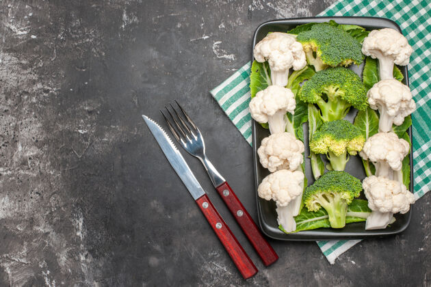 刀俯视生花椰菜和花椰菜在黑色矩形板上绿色和白色方格餐巾纸叉和刀在黑暗的表面自由的地方蔬菜方格顶部