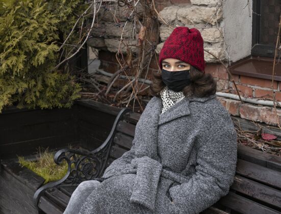 防护带着医用口罩的女人在户外的长凳上妇女病毒流行病