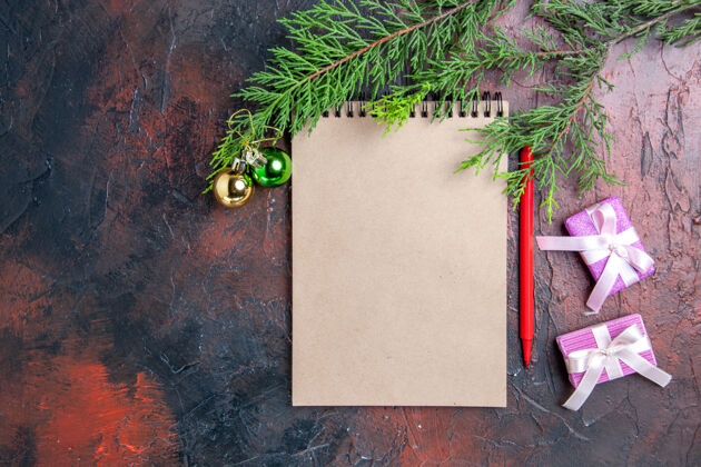 记事本顶视图红笔一个记事本松树树枝圣诞树玩具和礼物暗红色表面免费空间松树顶背景