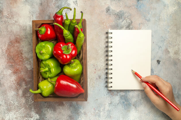 女士顶视图红色和绿色的辣椒辣椒在木箱笔记本铅笔在妇女手中裸体表面笔记本铅笔风景