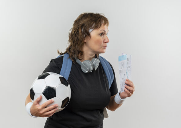 头带中年运动型女子 身穿黑色t恤 头上系着头带 背着背包 手里拿着机票和足球 站在白墙上 脸上挂着沉思的表情空气沉思足球