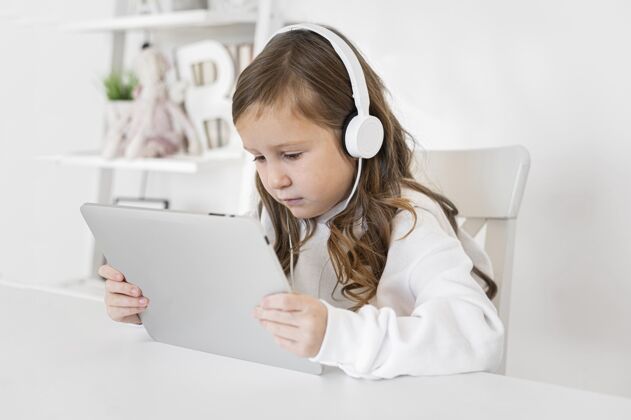 孩子女孩使用带耳机的平板电脑的侧视图设备女孩业余爱好