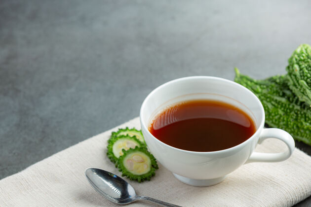 水一杯热的苦瓜茶 将生的苦瓜片放在白织物上蔬菜有益抗氧化剂