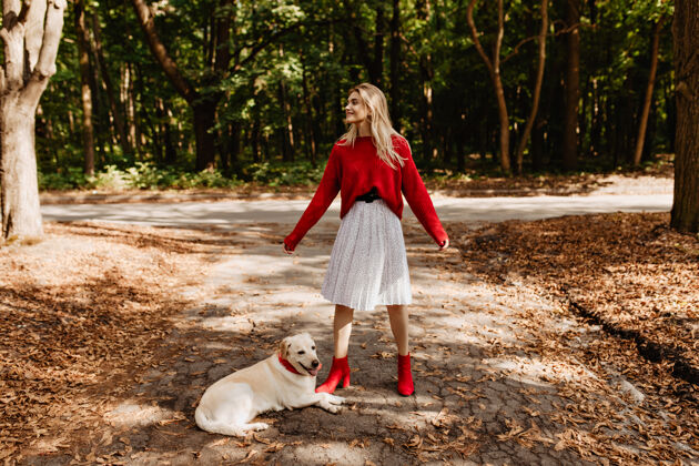 公园穿着红鞋子的时髦女孩和她的狗玩得很开心快乐的金发女郎在户外开心地笑着金发叶子户外