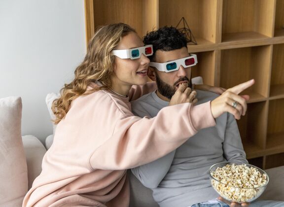 女朋友笑脸情侣在家里戴着立体眼镜看电影吃爆米花浪漫男朋友在一起