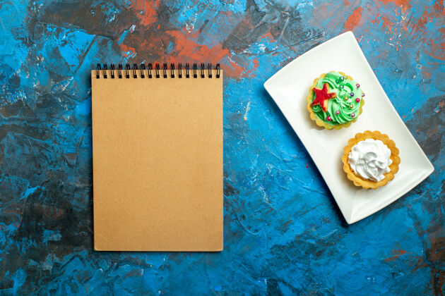 过期顶视图奶油馅饼在板笔记本上蓝红色的表面图版便笺顶部