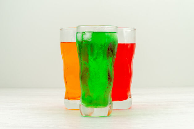 饮料正面视图白色表面上的长玻璃杯内五颜六色的果汁长玻璃杯新鲜
