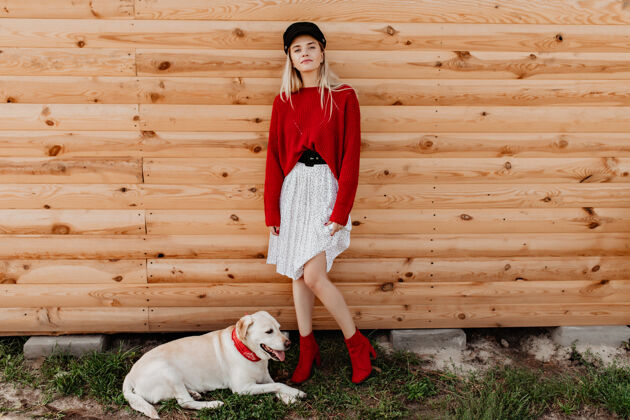 草穿着白色裙子和红色套头衫的漂亮金发女郎在木墙上摆姿势可爱的女孩在户外和她的狗在一起时感觉很平静很好金发微笑时尚