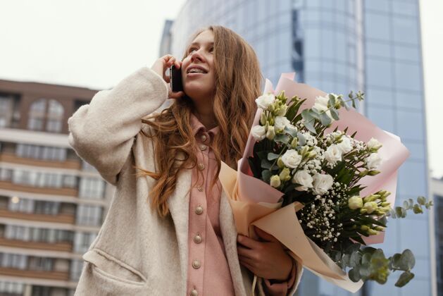 流动低角度的优雅女子在户外打电话 手持一束鲜花城市安排春天