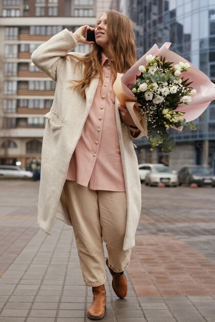 蔬菜户外优雅女士手持一束鲜花在电话中交谈的正面视图流动春天城市