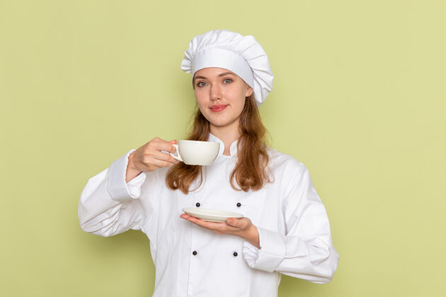 制服身着白色厨师服的女厨师手持杯子 微笑着站在绿色的墙上举行人套装
