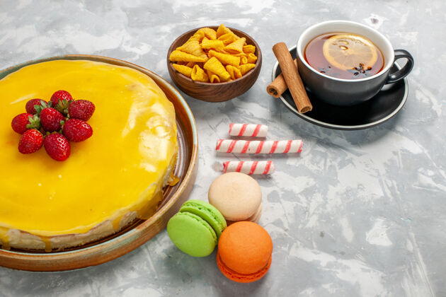 茶正面图黄色蛋糕 白色表面有麦卡龙和一杯茶杯子甜食水果