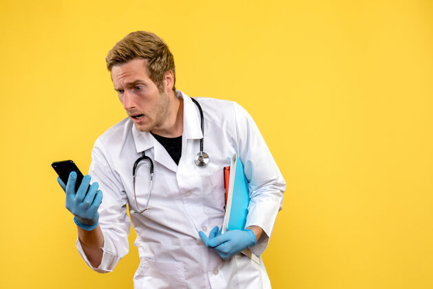 抱着正面图年轻男医生手持手机 背景为黄色病毒健康医护人员比赛护士病毒