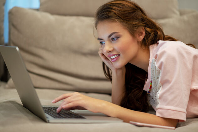 使用漂亮的女人在家拿着笔记本电脑年轻的女人坐在家里用电脑工作享受在家的时光房间撒谎看