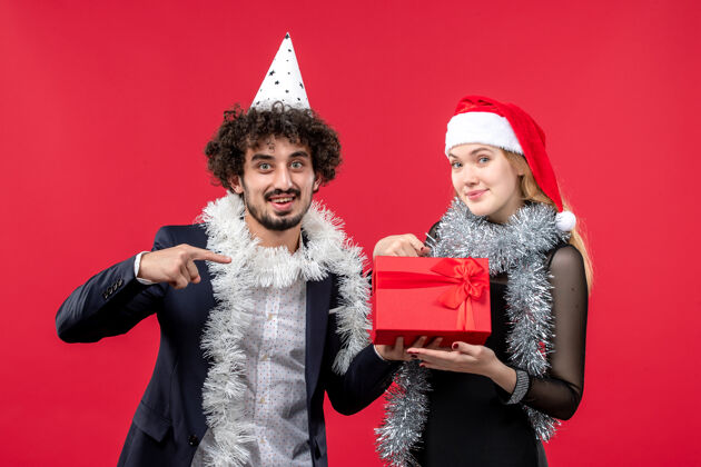 服装正面图年轻夫妇带着礼物在红墙派对上庆祝圣诞之爱风景圣诞节美丽