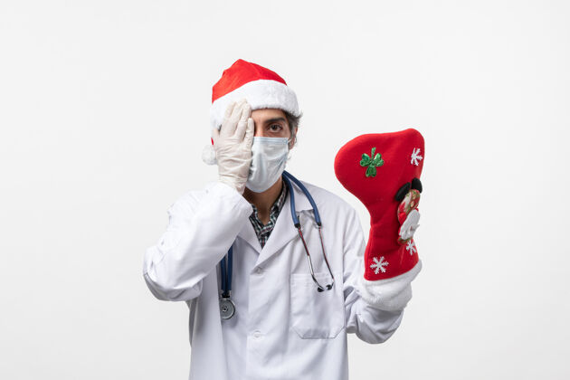 视图正面图男性医生拿着白色墙壁上的大节日袜子病毒柯维德-假日外套病毒圣诞节