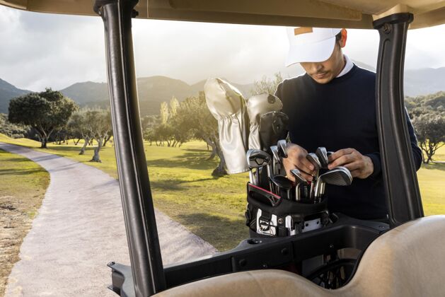 黄金高尔夫球车旁边拿着高尔夫球杆的男人的正视图男性娱乐户外