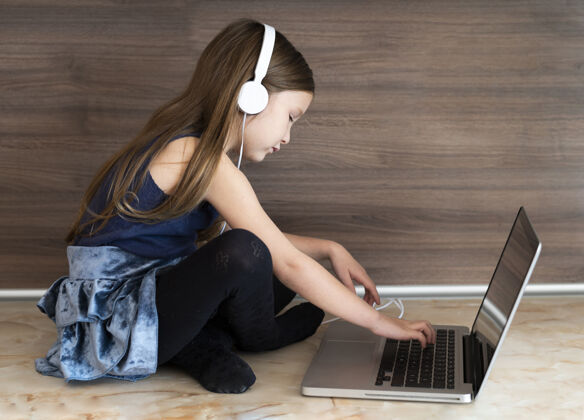 孩子女孩使用带耳机的笔记本电脑的侧视图年轻人设备年轻人