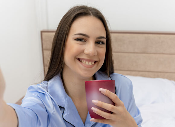 女人穿着蓝色睡衣躺在床上的年轻漂亮女人床咖啡杯子