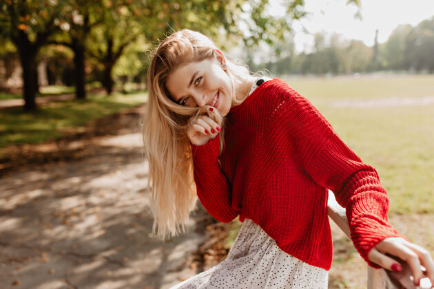 秋天快乐的年轻金发女郎 穿着时髦的红色毛衣和白色裙子 在秋天的公园里微笑着自然化妆的时髦女孩在户外摆姿势减肥成人漂亮