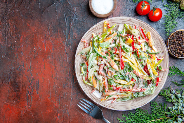 蔬菜顶视图蔬菜沙拉在盘子叉子上西红柿盐黑胡椒松枝在暗红色的桌子上复制空间绿色盘子一餐