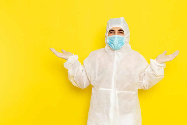 防护身穿白色特殊防护服 黄色墙壁上带无菌口罩的男性科学工作者的正面图危险肖像实验室外套