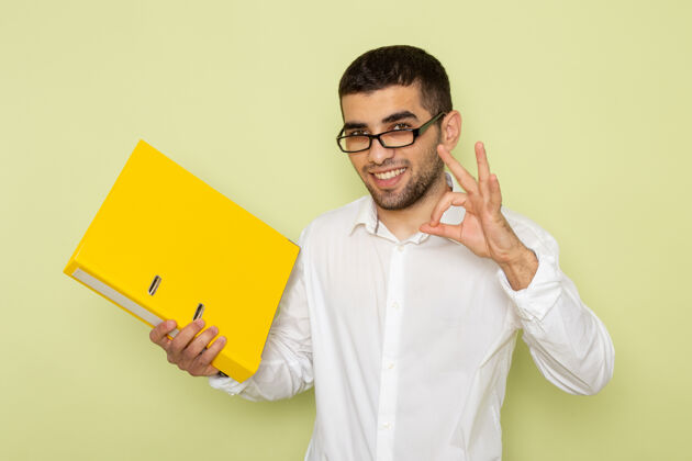 办公室身穿白衬衫的男办公室工作人员手持黄色文件 在浅绿色的墙上微笑成人肖像快乐