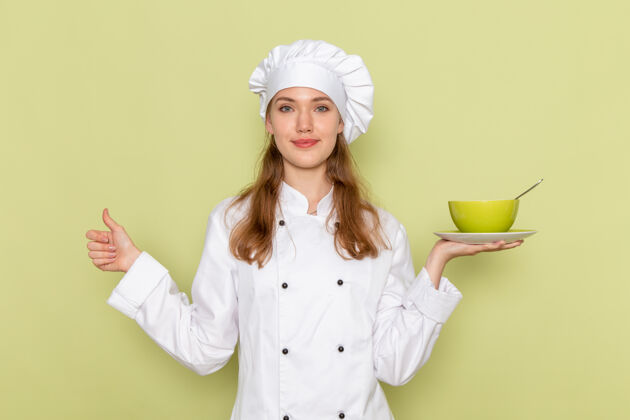 盘子女厨师身穿白色厨师服 手持绿色盘子 微笑着站在绿色的墙上专业淋浴女厨师