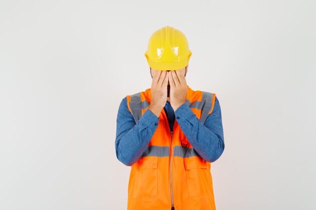 人年轻的建筑工人穿着衬衫 背心 戴着头盔 双手捂着脸 看上去很沮丧 正对着窗外工业背心封面