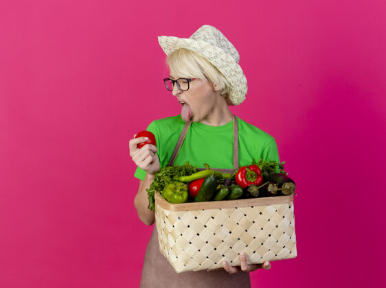 头发一位年轻的园丁 围着围裙 戴着帽子 手里拿着装满蔬菜的箱子满年轻蔬菜