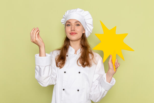 西装身穿白色厨师服的女厨师手持绿色墙壁上的黄色标志的正视图穿膳食烹饪