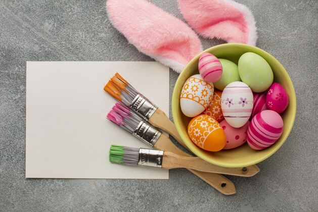 鸡蛋顶视图彩色复活节彩蛋在碗与油漆刷和兔子耳朵庆祝节日颜色
