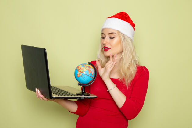 情绪正面图美丽的女性手持小地球仪和笔记本电脑在绿色的墙上圣诞彩雪节日新年感慨肖像视图圣诞节