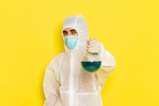 危险身穿特殊防护服的男性科学工作者的正面图 黄色墙上有带面罩的保温瓶防护健康医疗