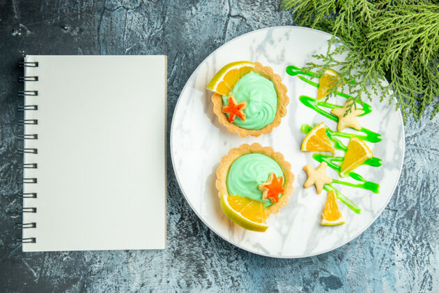 柠檬顶视图小馅饼与绿色糕点奶油和柠檬片板松枝记事本在黑暗的桌子上中国馅饼碗