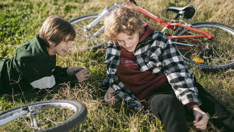 年轻笑脸男孩在草地上放松 而骑自行车自行车户外户外