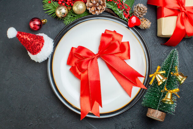 圆锥体上图：餐盘上的蝴蝶结红色丝带圣诞树冷杉枝针叶树锥礼盒圣诞老人帽黑色背景圣诞弓餐盘